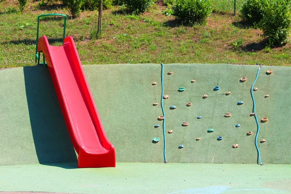 Rote Kunststoffrutsche Neben Der Kinderkletterwand Auf Dem Örtlichen Spielplatz Mit — Stockfoto