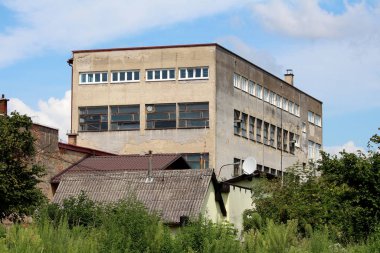 Aile evleri ve bulutlu arka planda yoğun ağaçlarla çevrili harap olmuş eski sanayi binası.