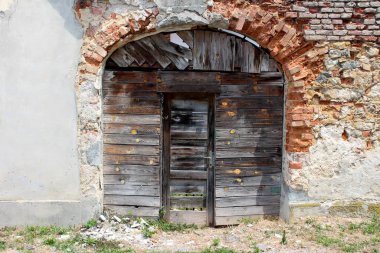 Terk edilmiş banliyö aile evinin arka bahçe girişi çatlamış ahşap tahtalar ve kırmızı tuğlalardan yapılmış dekoratif çerçevenin içinde ön tarafında çimen ve çakıl bulunan yıkık bir duvar parçası olarak küçük harap kapılar ile kapalı.