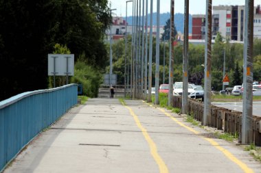 Arka planda sık ağaçlar ve apartman binaları ile çevrili uzun sokak lambaları ve işlek yol yan yana bisiklet rayı ile çatlamış kaldırım