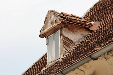 Kırık ahşap çerçeveli eski çatı penceresi. Terk edilmiş banliyö aile evinin kalıntıları. Gri gökyüzü arka planında çatılı kiremitlerle çevrili.