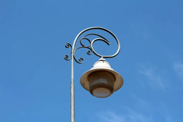 Baroque style street lamp with wrought iron decoration mounted on tall metal pole on clear blue sky background