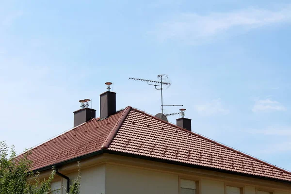 近代的な煙突と明確な青空の背景に改装された郊外の家族の家の上に複数のテレビアンテナと新しい屋根のタイル — ストック写真