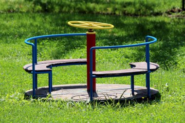 Kırık antika eski renkli açık hava oyun parkı ekipmanları metalden yapılmış ve köşe bucak olmuş ahşap şekilli yerel halk parkında kesilmemiş çimlerle çevrili.