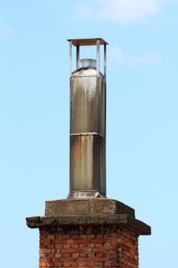 Üzerinde kısmen paslanmış ince metalden yapılmış metal kapaklı kirli eski sanayi bacası açık mavi gökyüzü arka planında kırmızı tuğla temeli