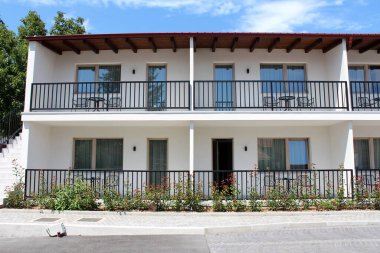 Yeni inşa edilmiş otel odası balkonları, siyah metal çitler ve dekoratif bahçe bitkileri ve çimento kaplı otoparklarla çevrili açık hava mobilyaları.