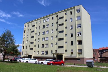 Yeni pencereleri ve açık yeşilden sarı cepheye çevrili, küçük banliyö aile evleri ve arka planda açık mavi gökyüzü olan büyük, yenilenmiş bir apartman.