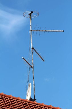 Beyaz elektrik kablolarına bağlı çeşitli boyutlarda TV ve radyo antenleri temiz mavi gökyüzü arka planındaki yeni banliyö aile evinin çatısında tek güçlü metal direğe monte edilmiş.