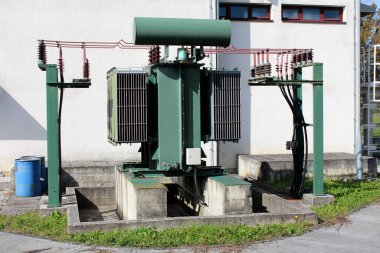 Çevresindeki çimenler ve asfalt kaldırımlarla çevrili beton temele monte edilmiş yerel elektrik santralinde çoklu bağlantılı elektrik kablolarına sahip eski moda vintage transformatör.