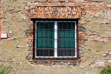 Tadilattan geçirilmiş eski çift camlı beyaz ahşap çerçeveli güçlü metal parmaklıklarla kaplı eski kırmızı tuğlalı aile evinin duvarına monte edilmiş ve şehrin eski bölümündeki çatlak cepheli.