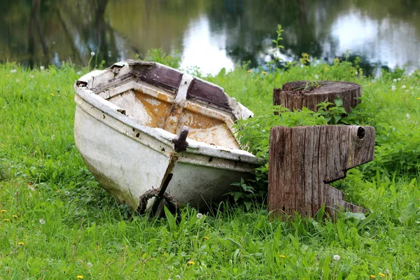 废弃的老式复古复古玻璃纤维船 残破的油漆残留在当地河岸的树桩旁 看起来像张奇怪的笑脸 周围环绕着未经修剪的草地和背景平静的河流 — 图库照片