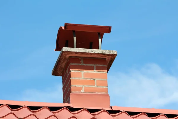 红色建筑砖烟囱 有波浪形盖 安装在新的郊区家庭住房屋顶瓦之上 蓝天背景清晰 — 图库照片