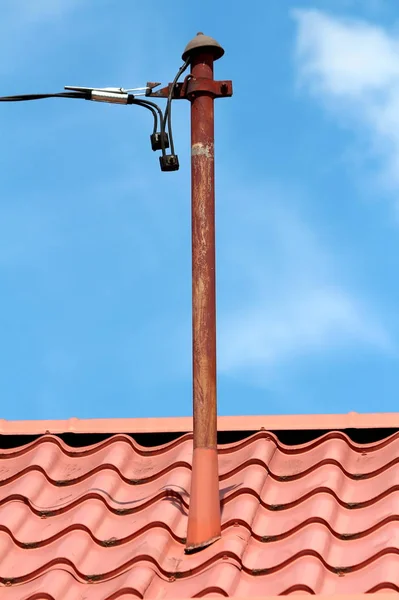 带有保护帽的锈蚀旧金属杆 装有新的黑暗电线 安装在明澈蓝天背景的郊区家庭住宅新屋顶瓷砖上 — 图库照片