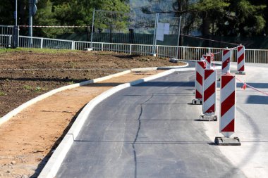Yeni döşenmiş asfalt yol hala inşaat halinde. Yeni beton kaldırımlar ve yerel inşaat alanında tamamlanmamış kaldırımlarla çevrili kırmızı ve beyaz uyarı levhalarıyla dolu.
