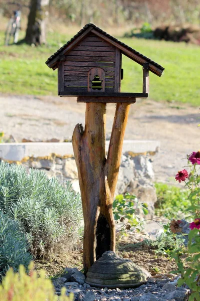 花や草に囲まれた郊外の家族の家の裏庭に木の切り株の上にフロントポーチと木製の丸太小屋の形で作られたレトロ素朴な新しく作られた装飾的な木製の鳥の家 — ストック写真