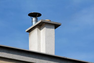Parlak metal kaplamalı beton beyaz baca ve temiz mavi arka plandaki eski banliyö aile evinin tepesinde koruyucu başlık.