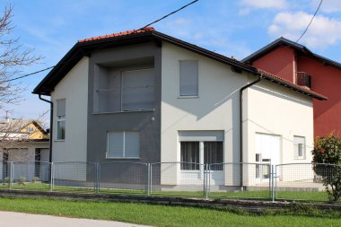 Beyaz ve gri yeni inşa edilmiş banliyö aile evi. Bitmemiş balkonları metal çitlerle çevrili ve güneşli bir sonbahar gününde taze kesilmiş çimenler.