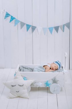 cute newborn baby in hat sleeping in wooden baby cot with star pillow near by  clipart