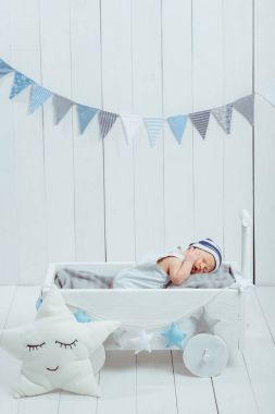 cute newborn baby in hat sleeping in wooden baby cot with star pillow near by  clipart