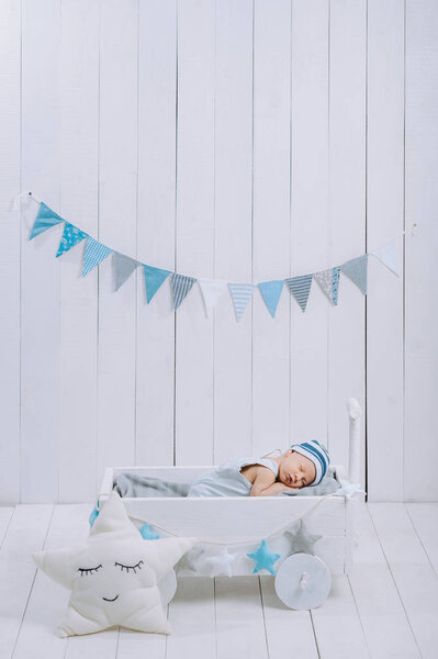cute newborn baby in hat sleeping in wooden baby cot with star pillow near by 