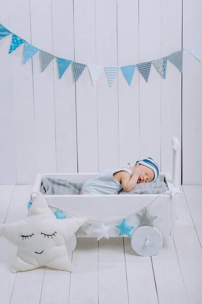 cute newborn baby in hat sleeping in wooden baby cot with star pillow near by 