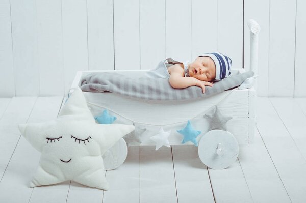 портрет очаровательного младенца в шляпе, спящего в деревянной детской кроватке, украшенной звездами

