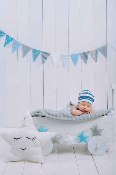 cute newborn baby in hat sleeping in wooden baby cot with star pillow near by 