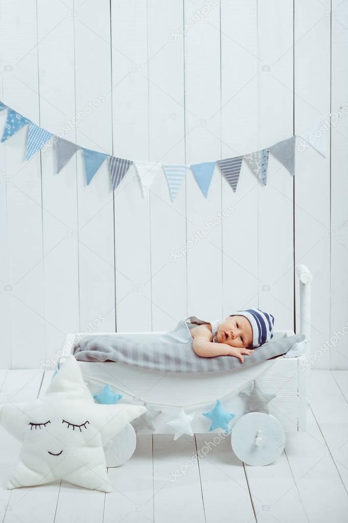 adorable infant baby in hat resting in wooden baby crib decorated with stars