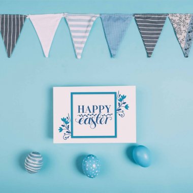 Mutlu Paskalya yazı ve Paskalya ile tebrik kartı üstten görünüm mavi yüzey üzerinde yumurta