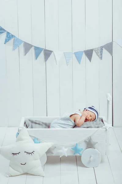 Cute newborn baby in hat sleeping in wooden baby cot with star pillow near by — Stock Photo