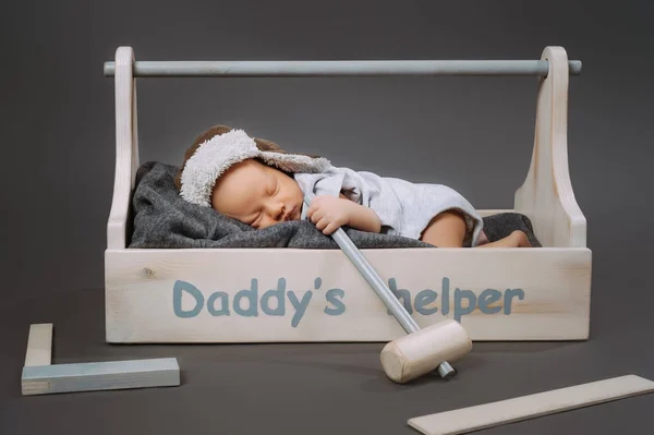 Adorable bébé avec marteau à la main dormant dans une boîte à outils en bois avec lettrage daddys helper — Photo de stock