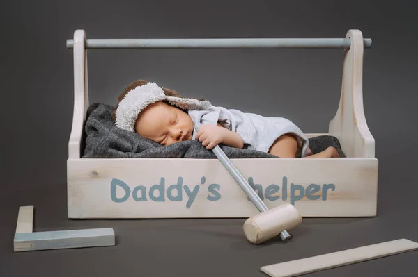 Adorabile bambino con martello in mano dormire in cassetta degli attrezzi di legno con daddys helper lettering — Foto stock