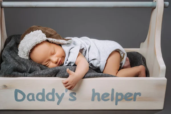 Cute infant baby showing thumb up while sleeping in wooden toolbox with daddys helper lettering — Stock Photo