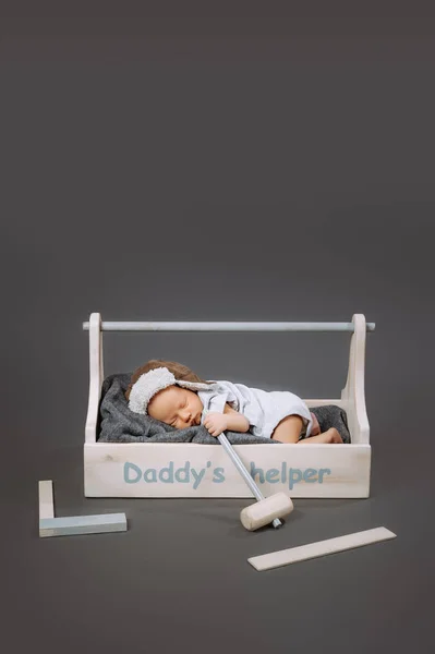 Bebê adorável com martelo na mão dormindo em caixa de ferramentas de madeira com daddys letras ajudante — Fotografia de Stock