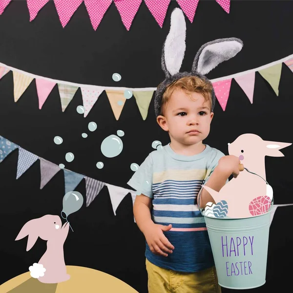 Adorable little kid with bunny ears and bucket on black, happy easter lettering and bunnies collage — Stock Photo