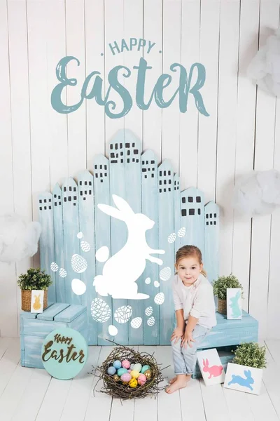 Adorable little child sitting in easter decorated room with happy easter lettering — Stock Photo