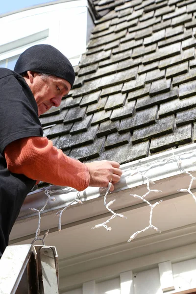 Vertikaler Mann auf Leiter hängt Weihnachtsbeleuchtung auf — Stockfoto