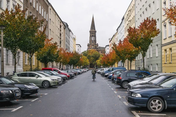 Berlijn - 19 oktober 2016: Man op een fiets rijden in een straat met kleurrijke bomen en Zionskirche kerk in het midden. — Stockfoto