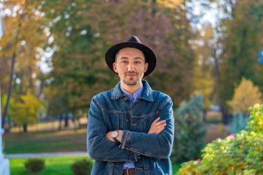 Yakışıklı genç adam kameraya bakıyor. Dışarıda kot ceketli ve mavi gömlekli kendinden emin ve başarılı bir gencin portresi. Mutlu adam gülümsüyor.