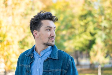 Dışarıda kot ceketli ve mavi gömlekli kendinden emin ve başarılı bir gencin portresi. Dışarıdaki yakışıklı genç adam. Mutlu adam gülümsüyor.