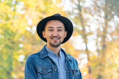 Yakışıklı genç adam kameraya bakıyor. Dışarıda kot ceketli, mavi gömlekli, kendinden emin ve başarılı bir gencin portresi. Mutlu adam gülümsüyor.