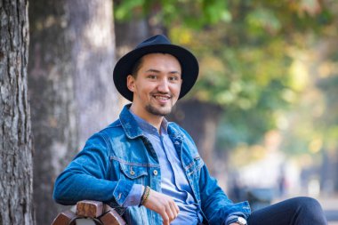 Yakışıklı genç adam kameraya bakıyor. Dışarıda kot ceketli, mavi gömlekli, kendinden emin ve başarılı bir gencin portresi. Mutlu adam gülümsüyor.