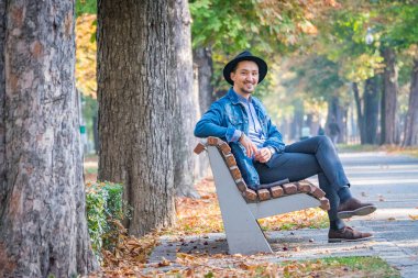 Yakışıklı genç adam kameraya bakıyor. Dışarıda kot ceketli, mavi gömlekli, kendinden emin ve başarılı bir gencin portresi. Mutlu adam gülümsüyor.