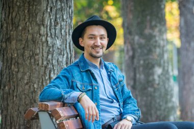 Yakışıklı genç adam kameraya bakıyor. Dışarıda kot ceketli, mavi gömlekli, kendinden emin ve başarılı bir gencin portresi. Mutlu adam gülümsüyor.