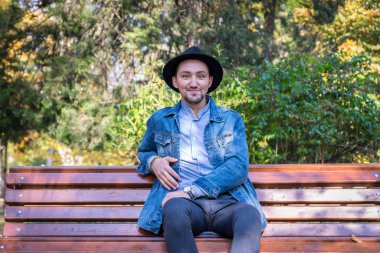 Yakışıklı genç adam kameraya bakıyor. Dışarıda kot ceketli ve mavi gömlekli kendinden emin ve başarılı bir gencin portresi. Mutlu adam gülümsüyor.