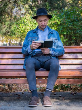 Parkta kitap okuyan yakışıklı bir delikanlı. Dışarıda kitap okuyan kot ceketli ve mavi gömlekli genç bir adamın portresi. Parkta kitap okuyan bir adam..