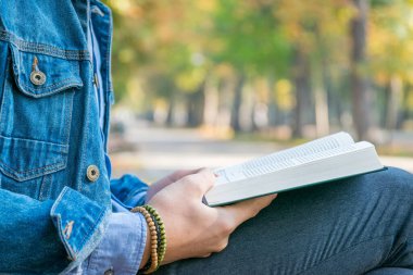 Parkta kitap okuyan yakışıklı bir delikanlı. Dışarıda kitap okuyan kot ceketli ve mavi gömlekli genç bir adamın portresi. Parkta kitap okuyan bir adam..