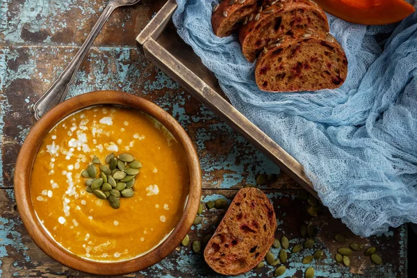 Bowl of traditional homemade pumpkin soup with seads, cream and bread on rustic wooden table — Stock Photo, Image