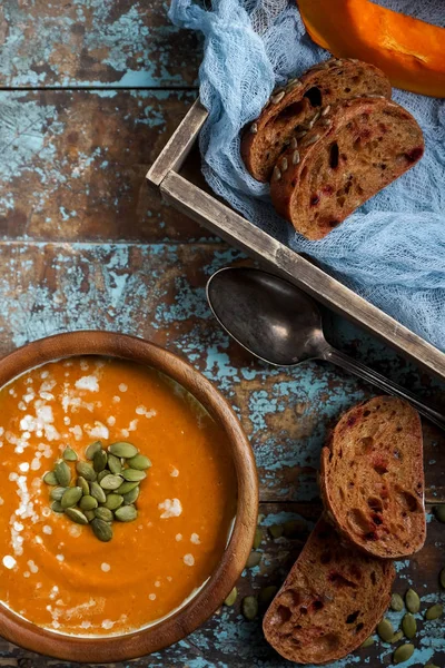 Bowl of traditional homemade pumpkin soup with seads, cream and bread on rustic wooden table — Stock Photo, Image