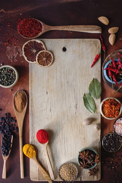 Varias especias indias en cucharas de madera, semillas, hierbas y nueces y tablero de madera vacío — Foto de Stock